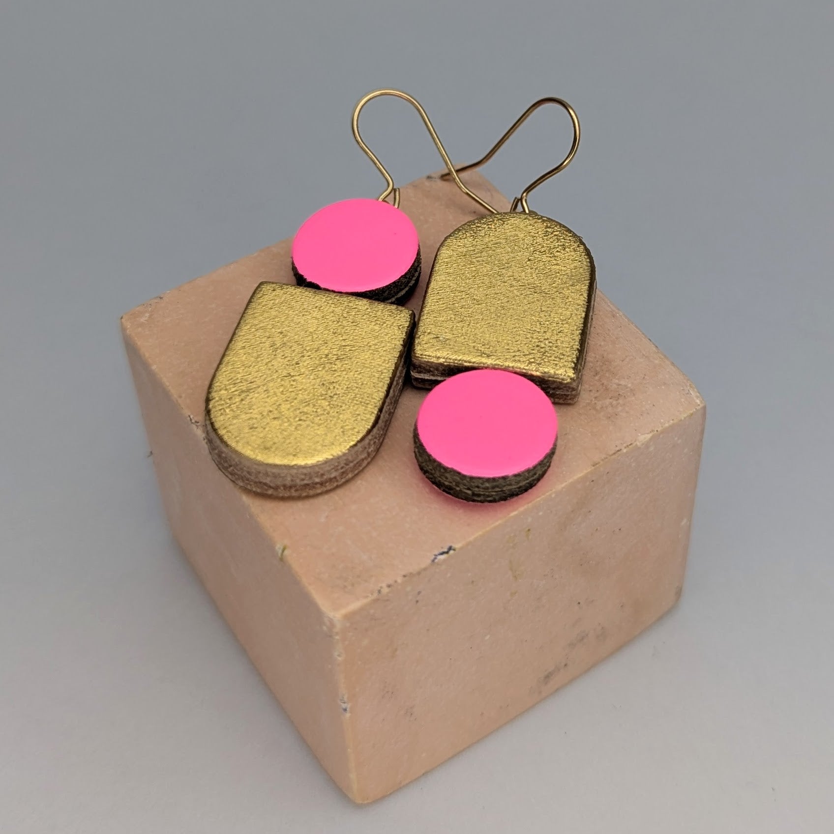 A pair of gold-plated earrings with fluoro pink and gold leather by Kay Morgan, Bristol.